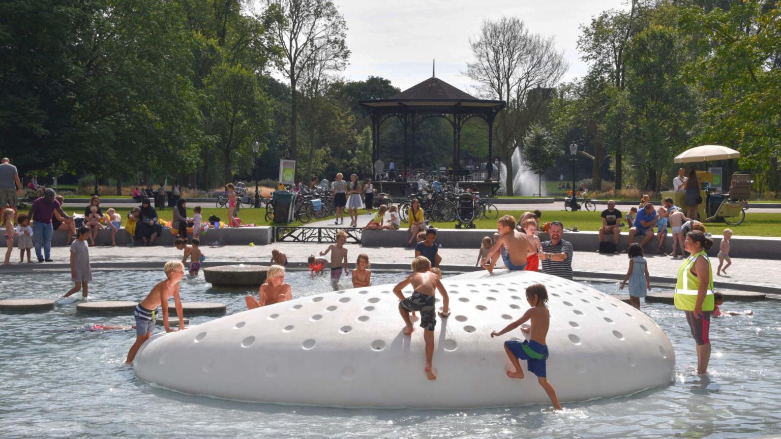 Children play in the water playground on a large stone in Oosterpark in Amsterdam.