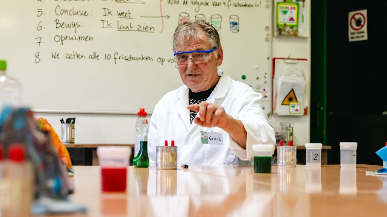 Een Hemlab-begeleider in labjas legt een experiment uit voor het whiteboard.