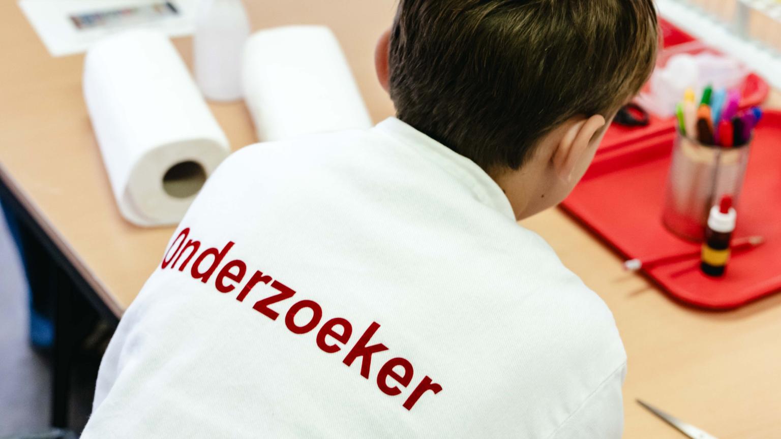 Kind met een labjas met het woord ‘Onderzoeker’ werkt aan een science-tafel.