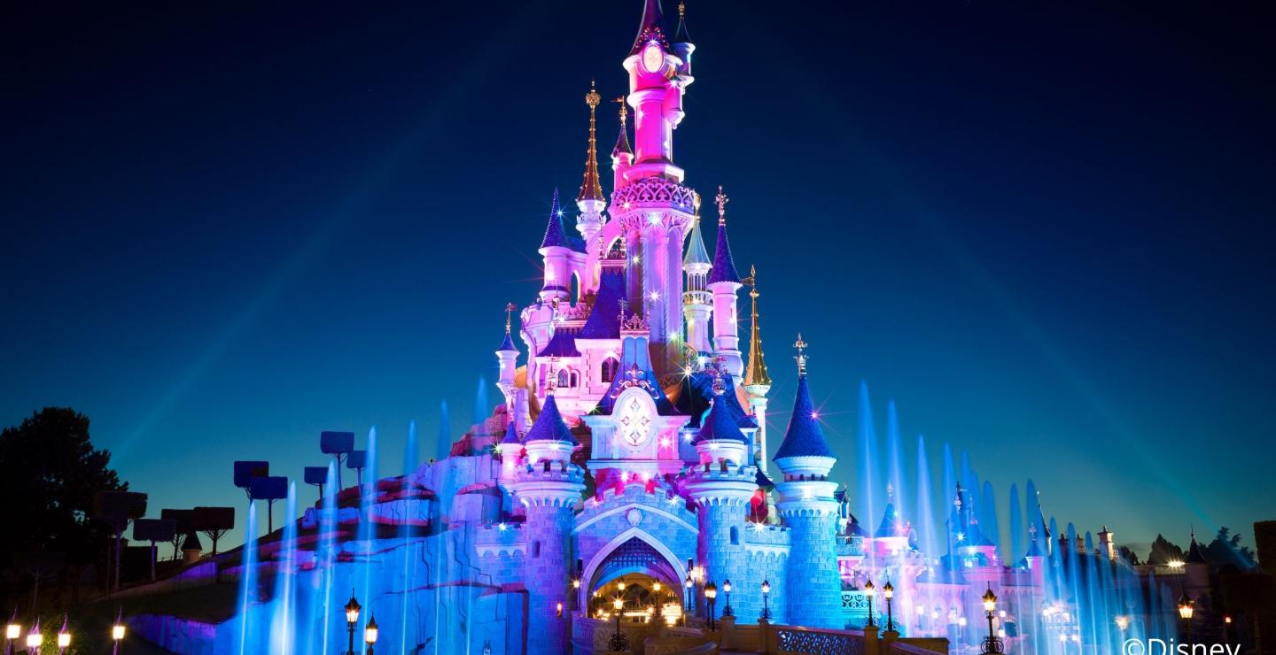 Verlicht Disneyland-kasteel in de avond met fontein en kleurrijke lichtprojecties