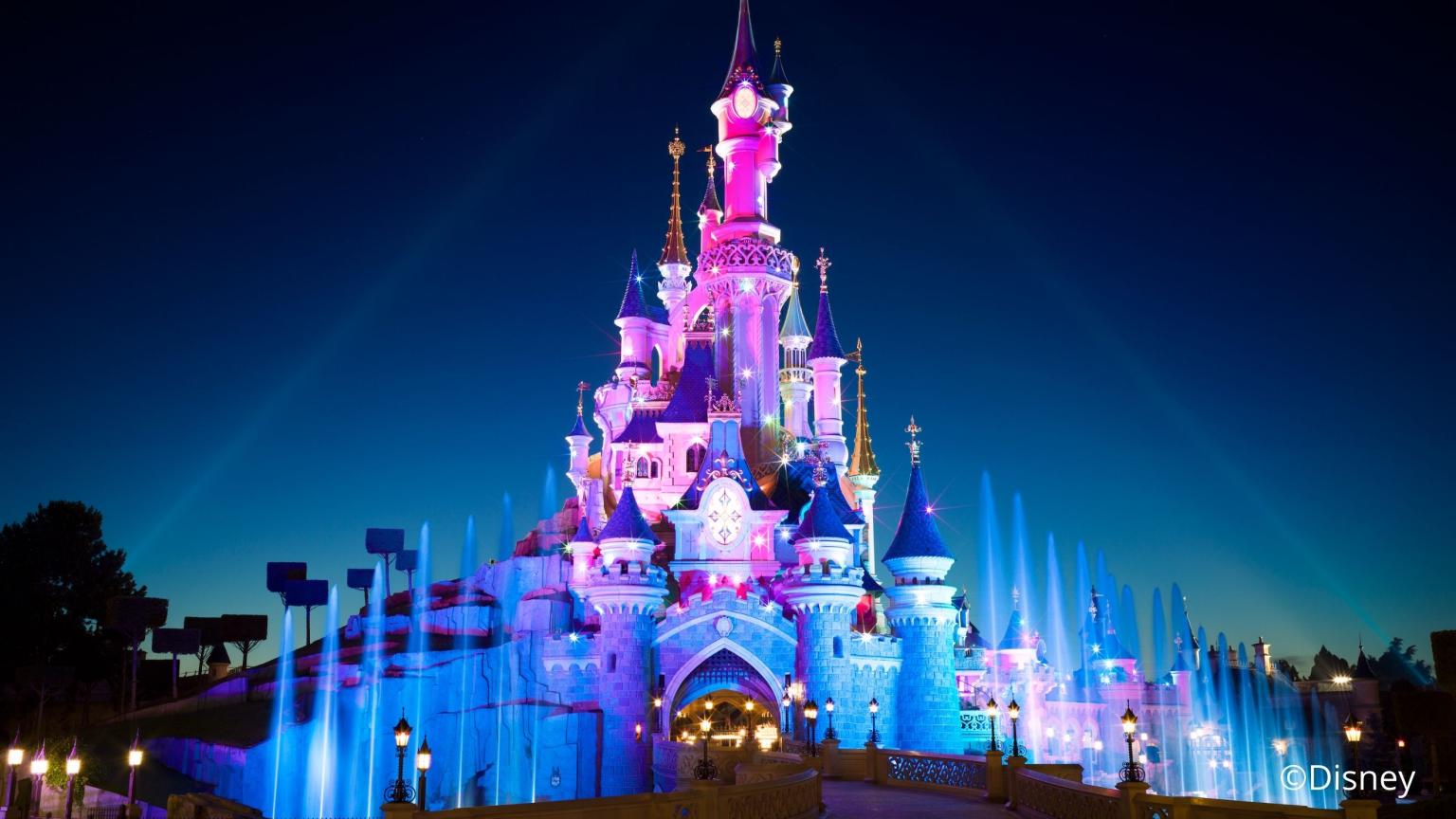 Illuminated Disneyland castle at night with fountains and colorful light projections