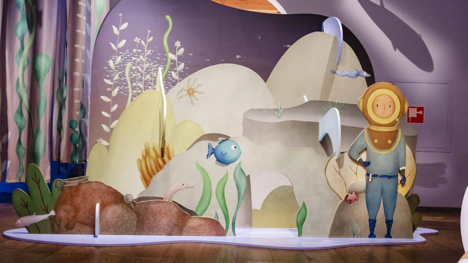 Illustratie van een onderwaterwereld met planten, vissen en het karakter Duiker Doris in duikerspak.