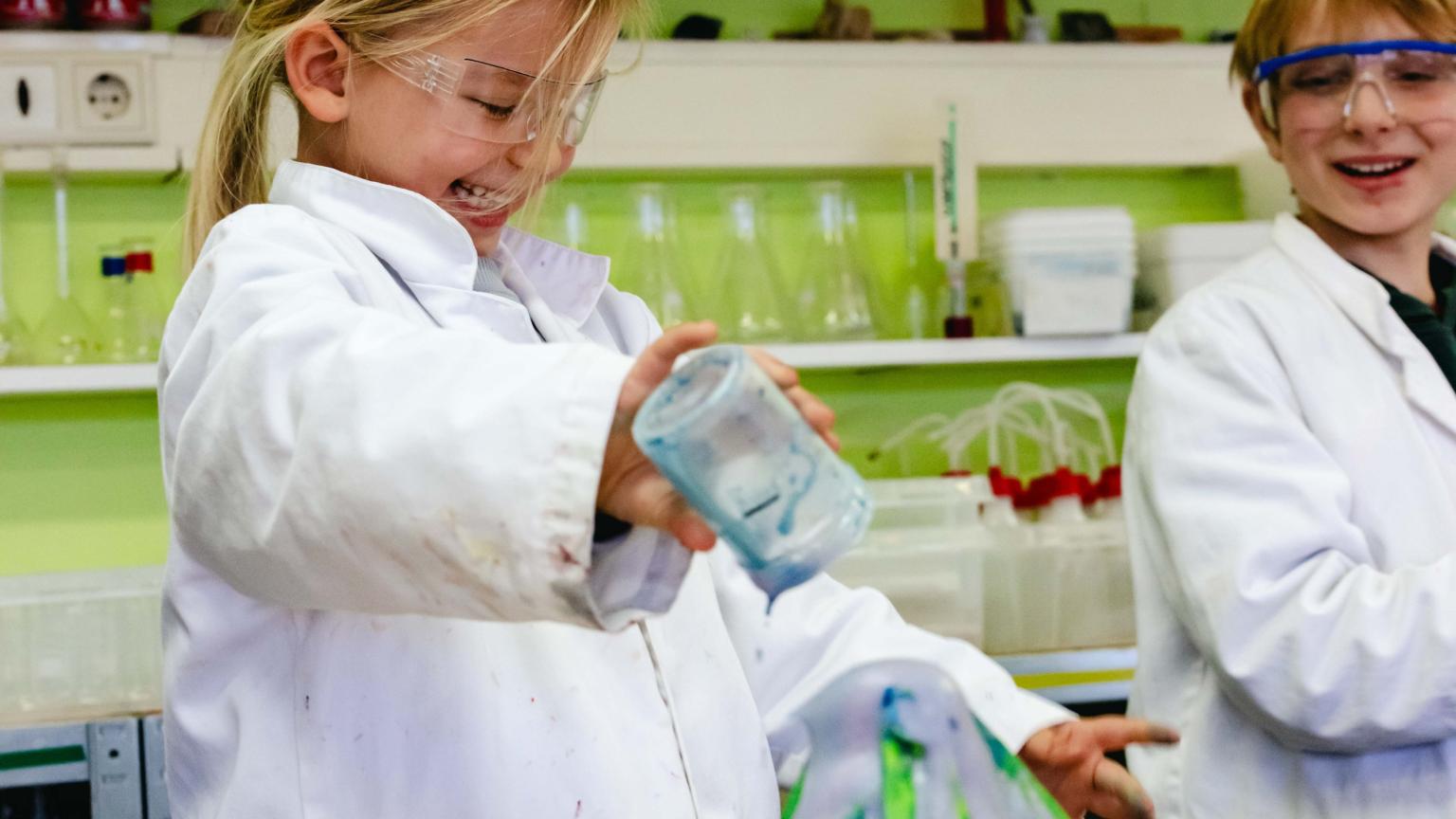 Smiling child conducting a science experiment with colored liquid during a workshop at Hemlab