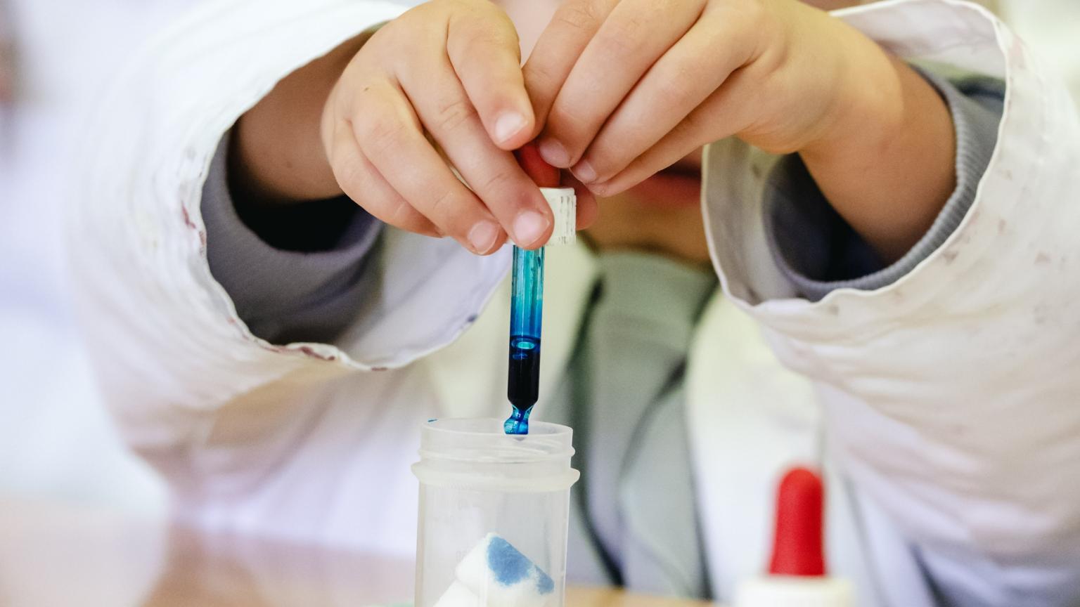 Close-up van kinderhanden die met een pipet vloeistof mengen tijdens een proefje