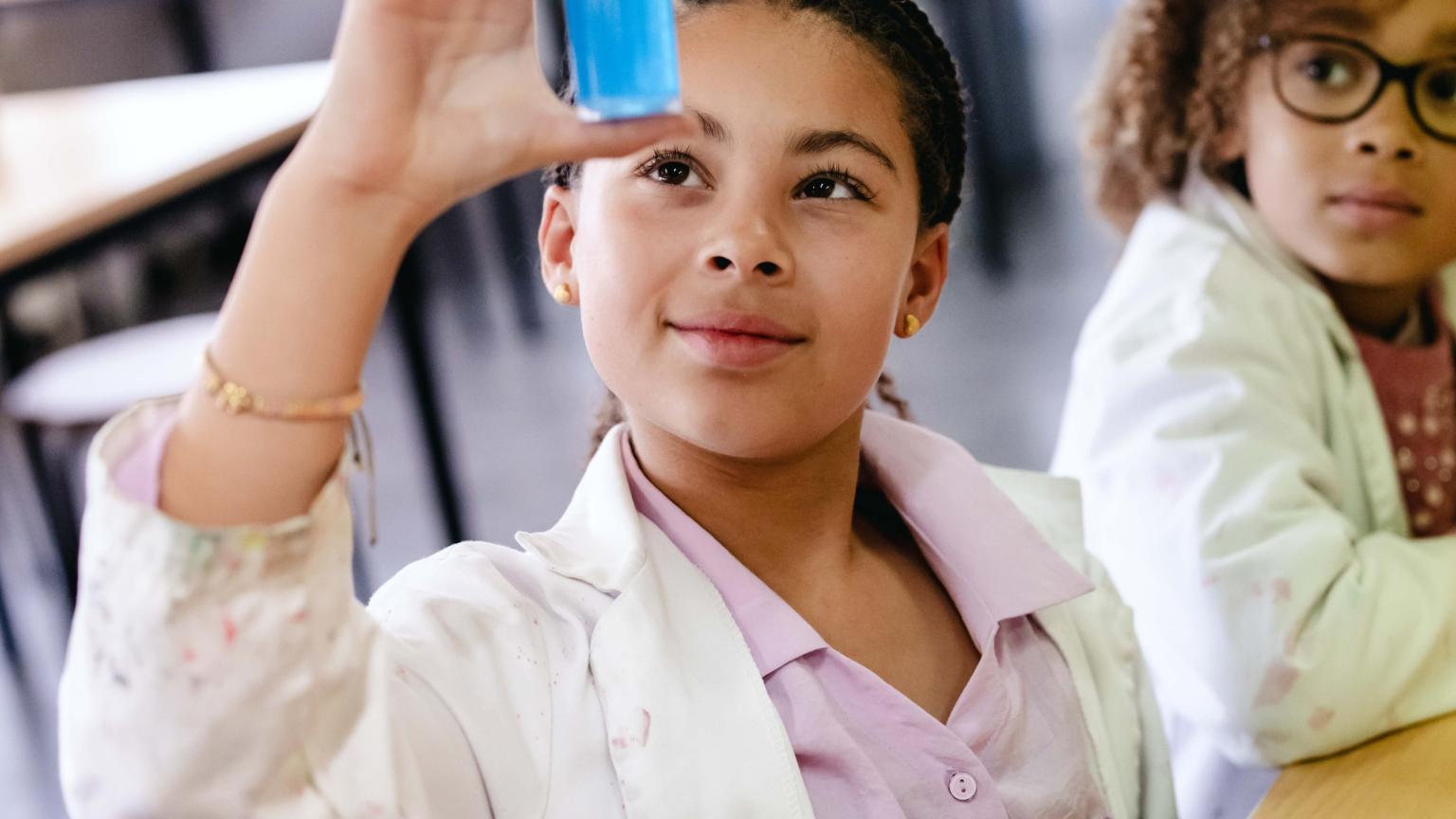 Een meisje observeert een reageerbuisje met blauwe vloeistof tijdens een proefje.