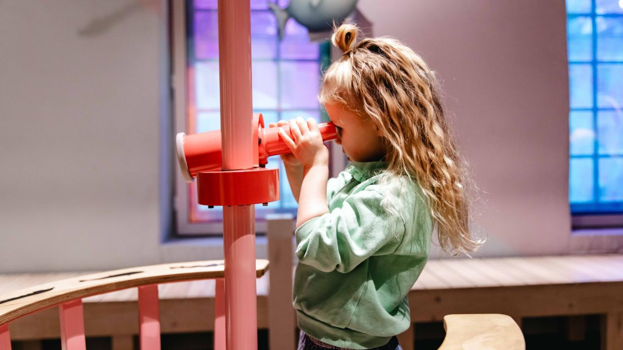 meisje kijkt door verrekijker bij tentoonstelling  Doris Duiker
                