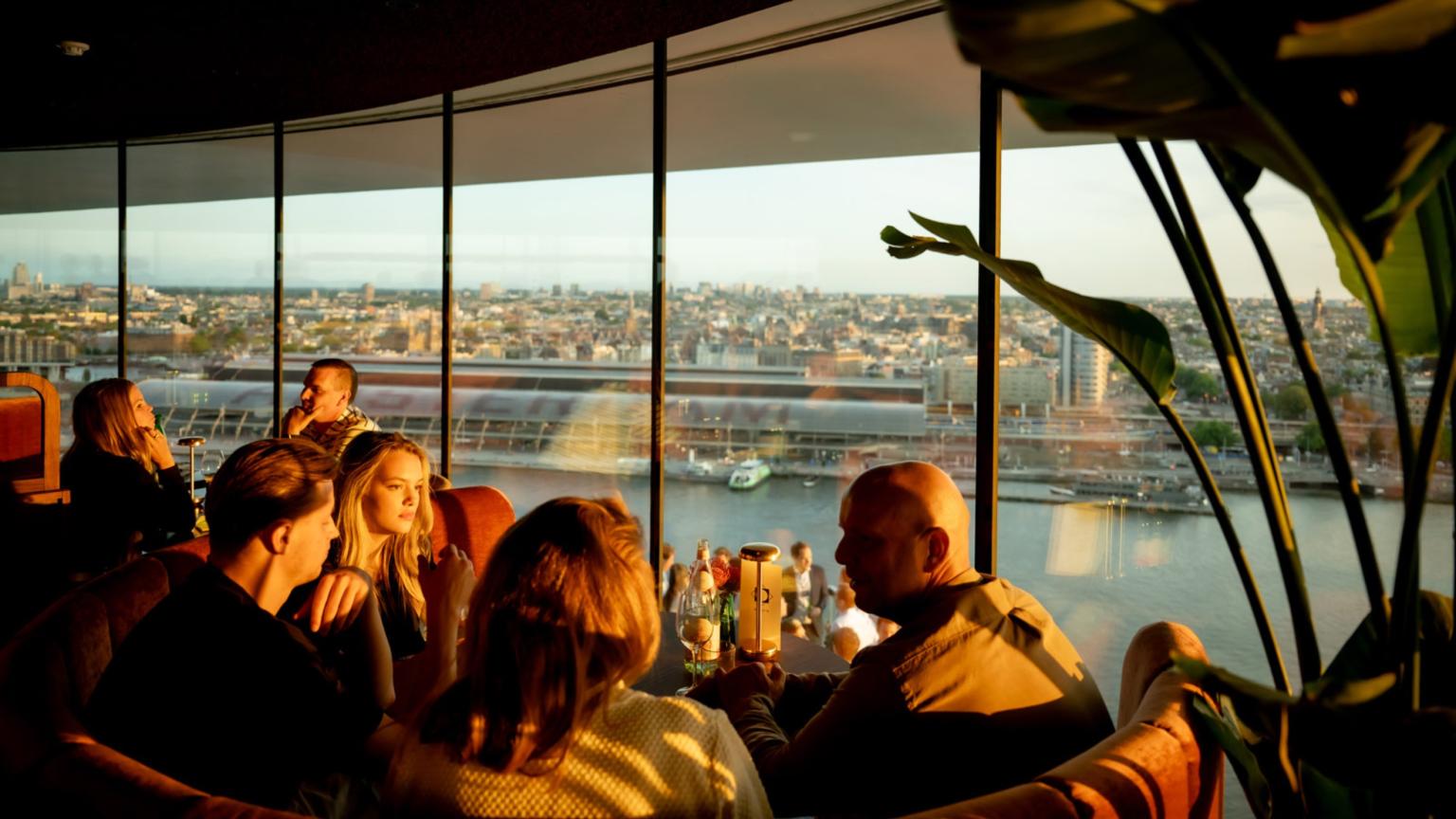 Bezoekers genieten van het uitzicht over de stad vanuit de binnenruimte van A’DAM Lookout.