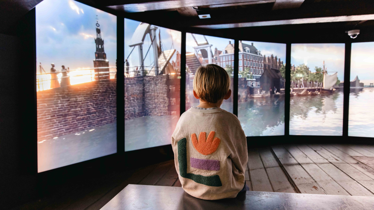 Kind dat aan boord van het VOC-schip Amsterdam naar een projectie kijkt over hoe het leven in Amsterdam er vroeger uitzag.