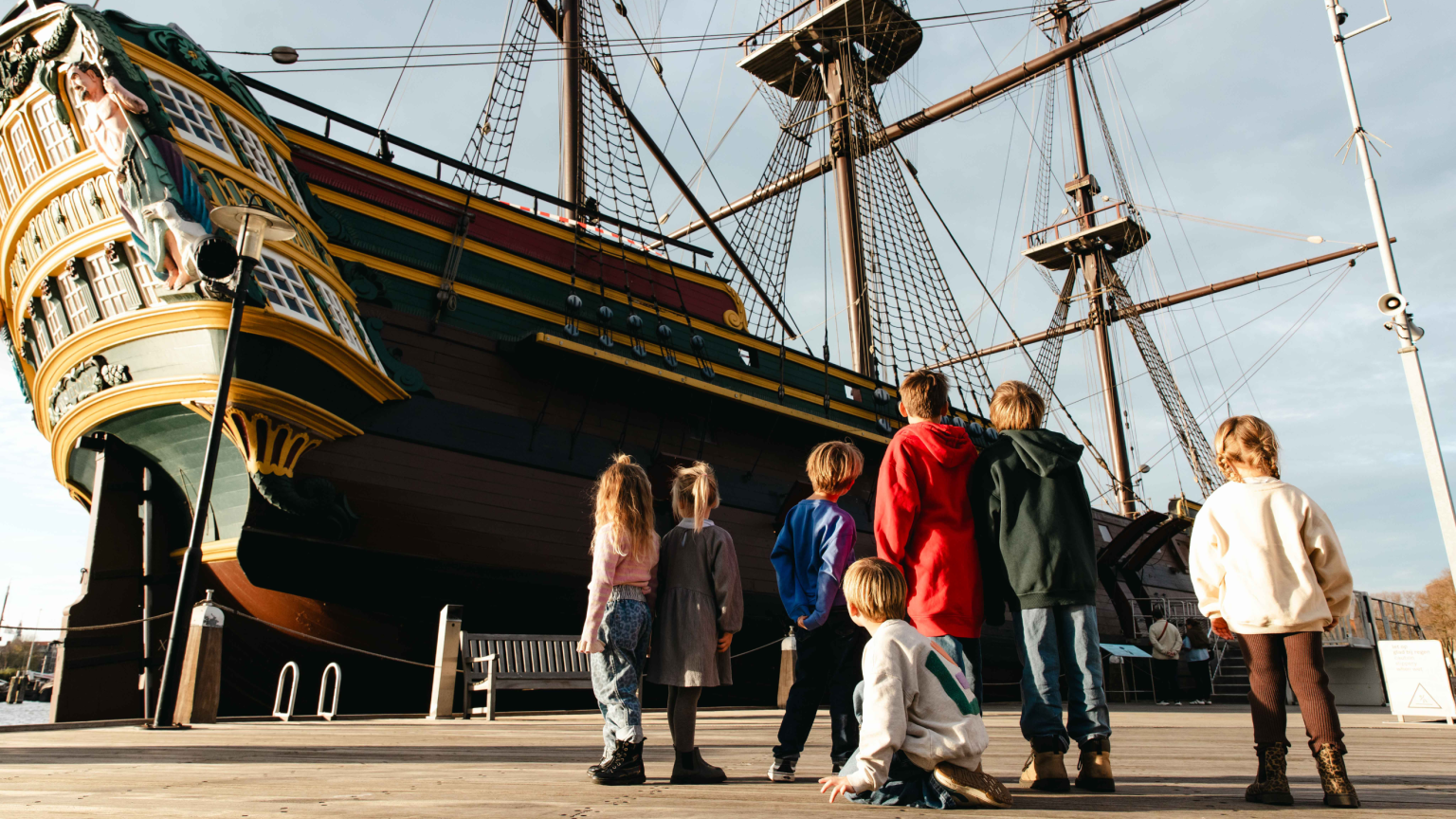 kinderen kijken naar het VOC-schip Amsterdam aan de steiger bij Het Scheepvaartmuseum
