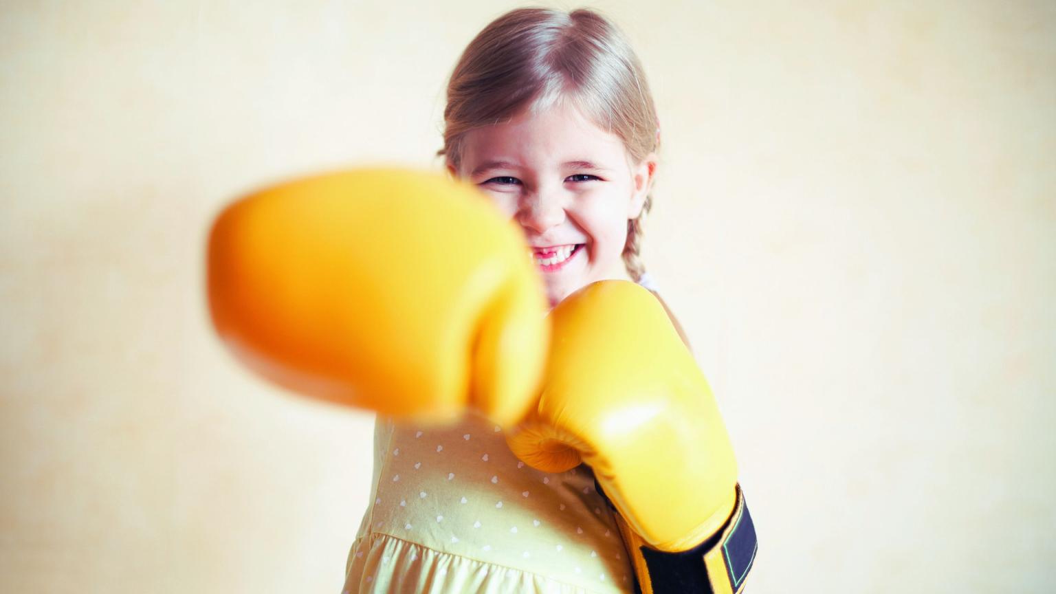 Lachend kind met gele bokshandschoenen een self-defenseles bij WOW Family Center.