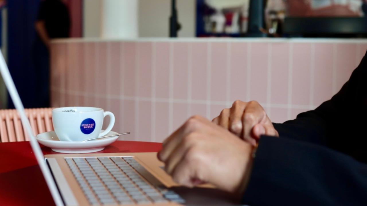 Iemand werkt op een laptop in een café met een kop koffie op tafel | playtix
                