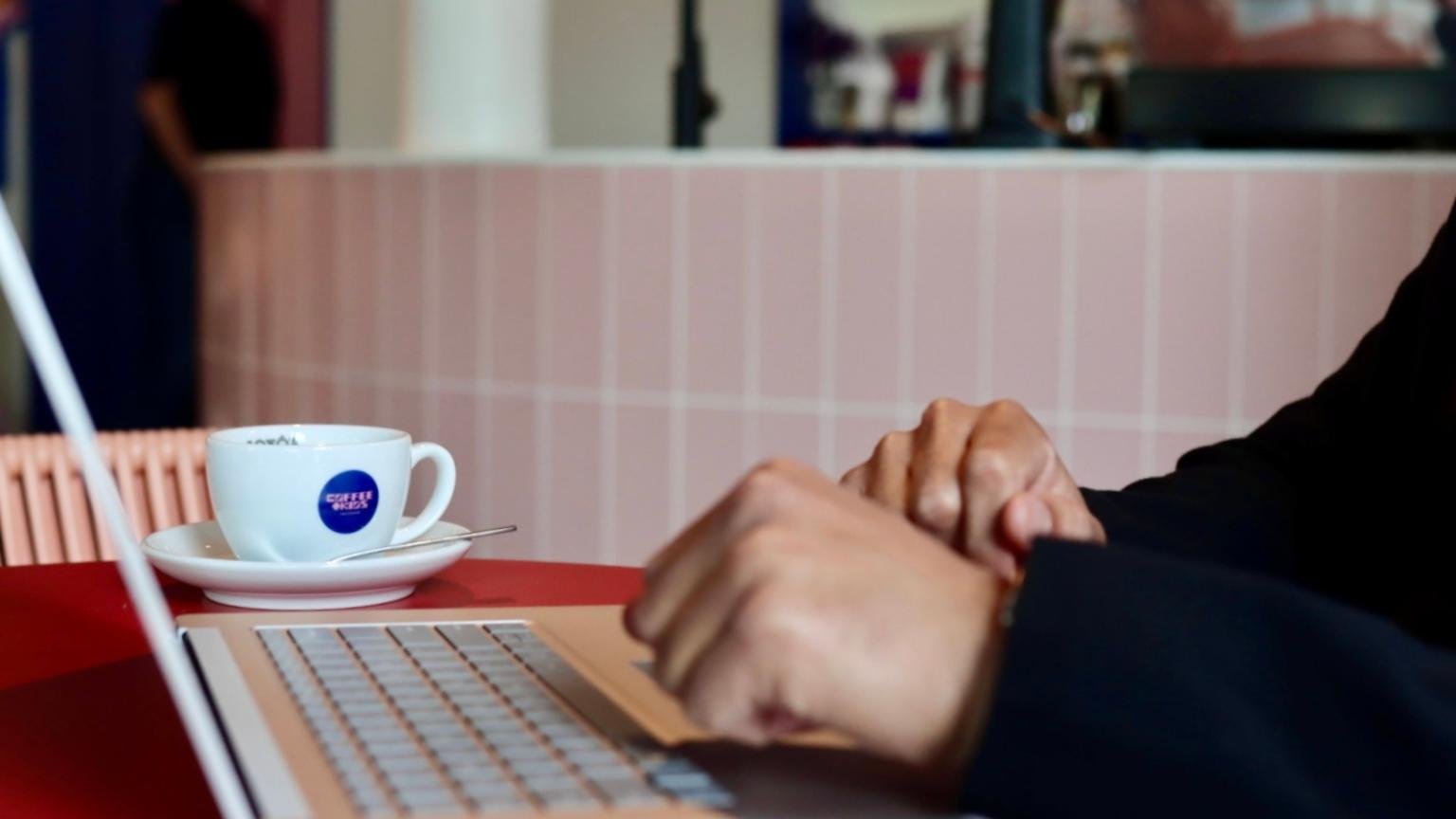 Iemand werkt op een laptop in een café met een kop koffie op tafel | playtix