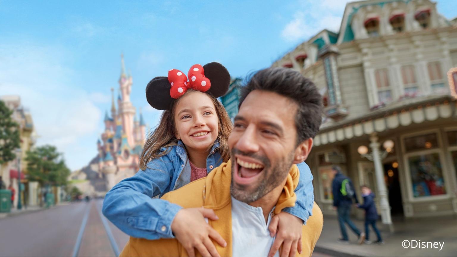 Father carrying his daughter wearing Mickey Mouse ears on Main Street in Disneyland with castle in the background