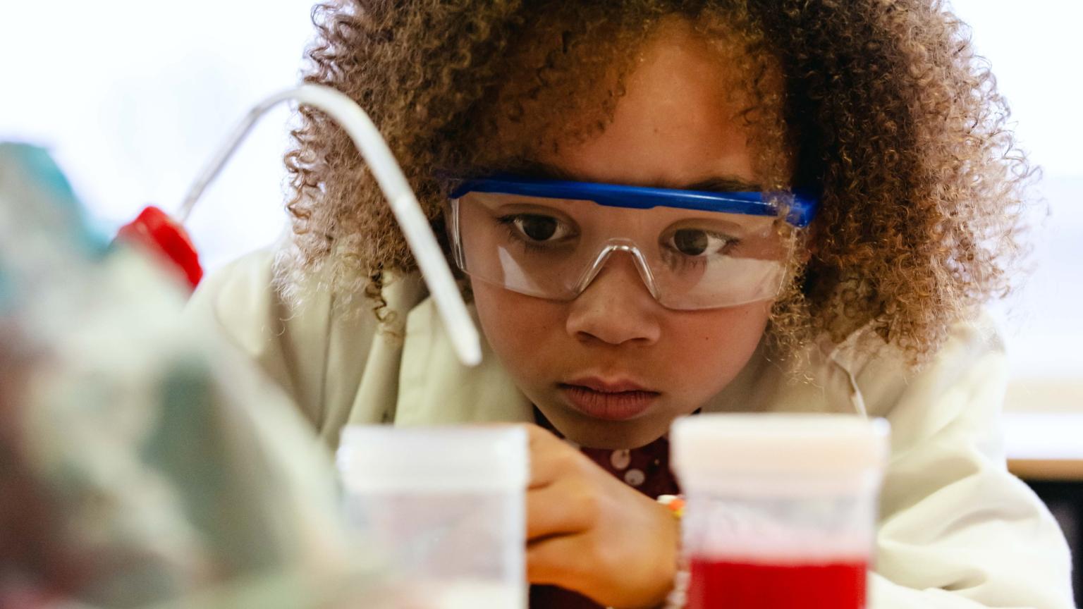 Curious girl wearing safety goggles observing a science experiment at Hemlab